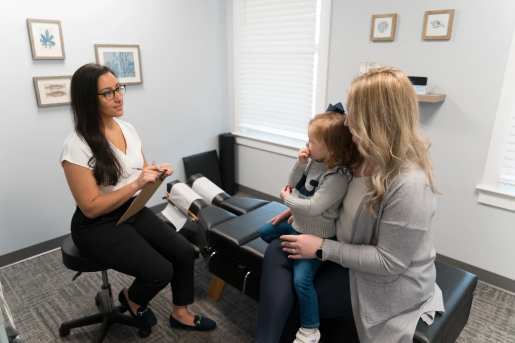 A woman and child sit in a chair with Chiropractor to get an evaluation.