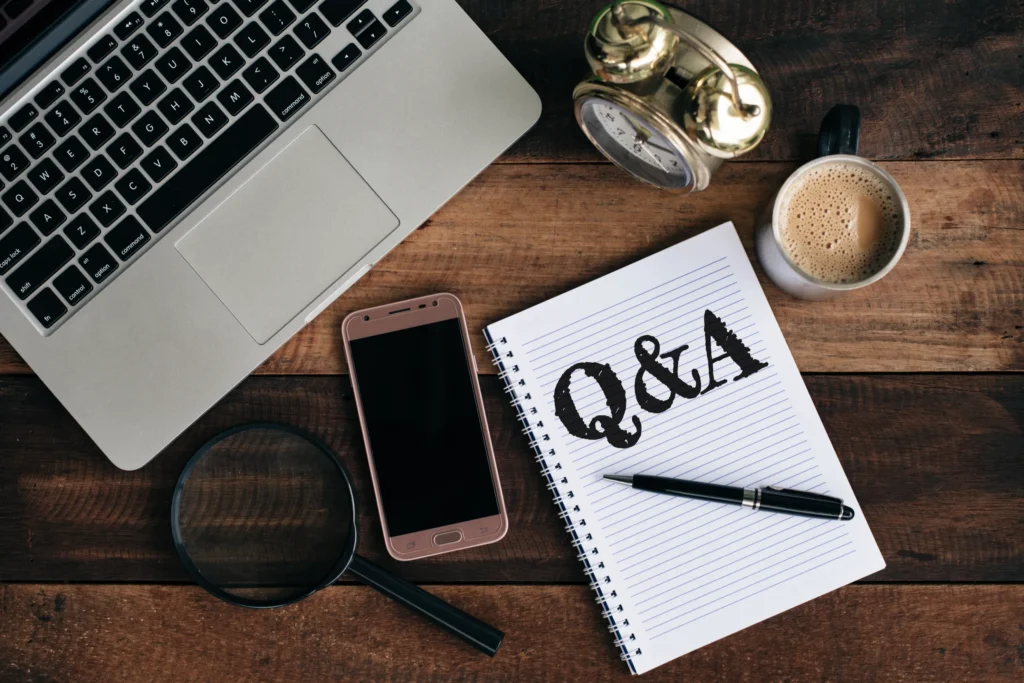Image of laptop, phone, clock, coffee and magnifying glass with a notepad that says Q&A
