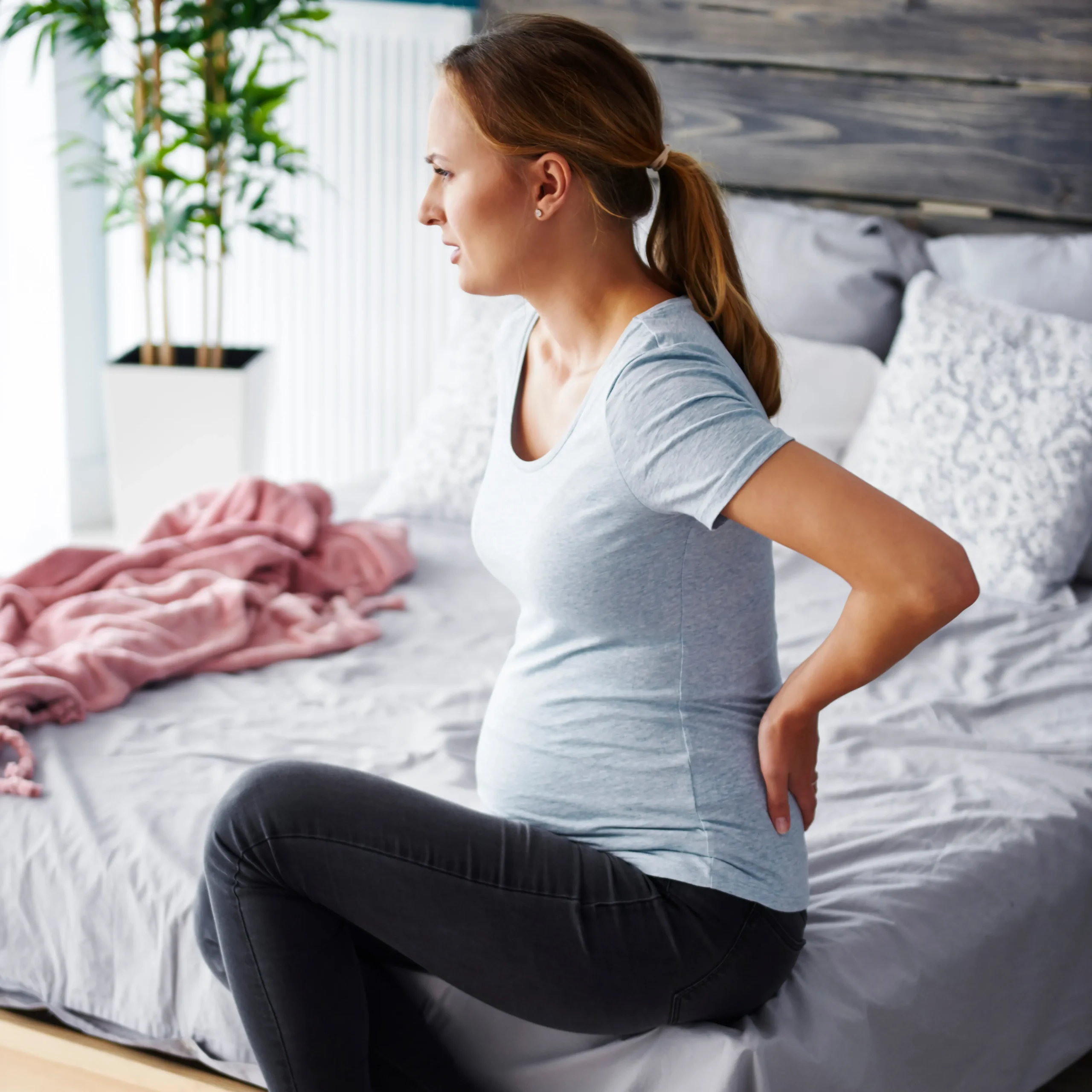 Pregnant woman sitting on a bed, viewed from behind, contemplating chiropractic safety during pregnancy.
