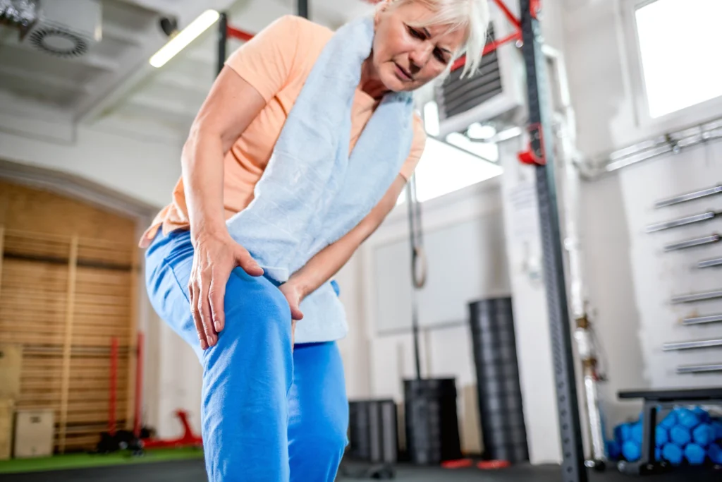 An older woman grips her knee in a gym, representing the focus on mobility and wellness at MCR Chiropractic. Symbolizing the journey to improved mobility and health through chiropractic care.