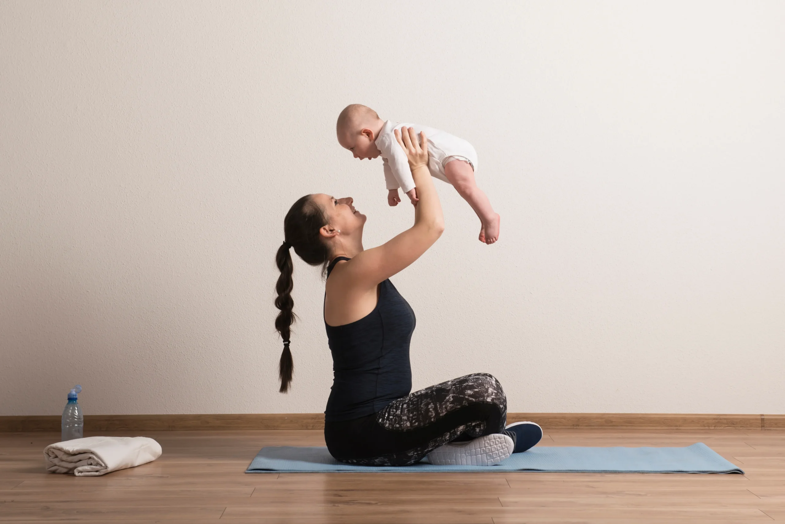 A mother holds her baby aloft during yoga, illustrating the harmony of motherhood and the benefits of chiropractic care.