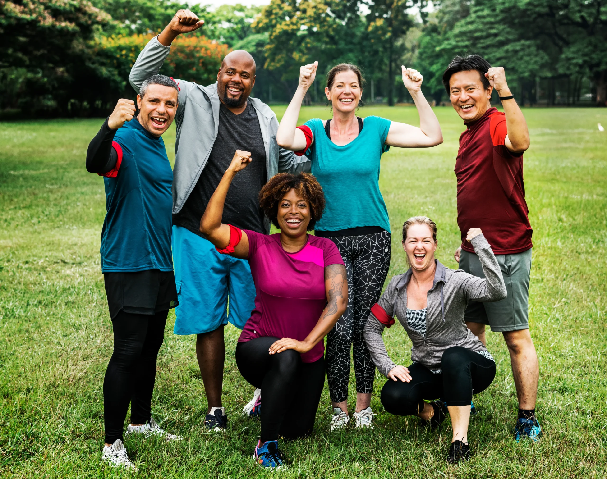 group of six People in a park with arms raised, celebrating health and vitality through chiropractic care for lifelong movement.