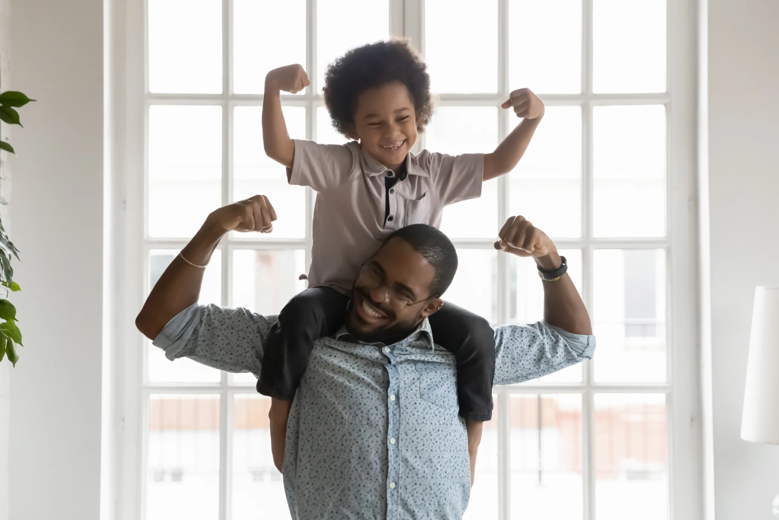 Father carrying child on shoulders flexing bicep's and laughing.
